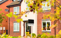 Ownership and Real Estate Property investment UK Red brick family house For Sale sign and front yard in suburban peaceful neighborhood Welcoming house facade with green lawn seen through foliage 2732910525